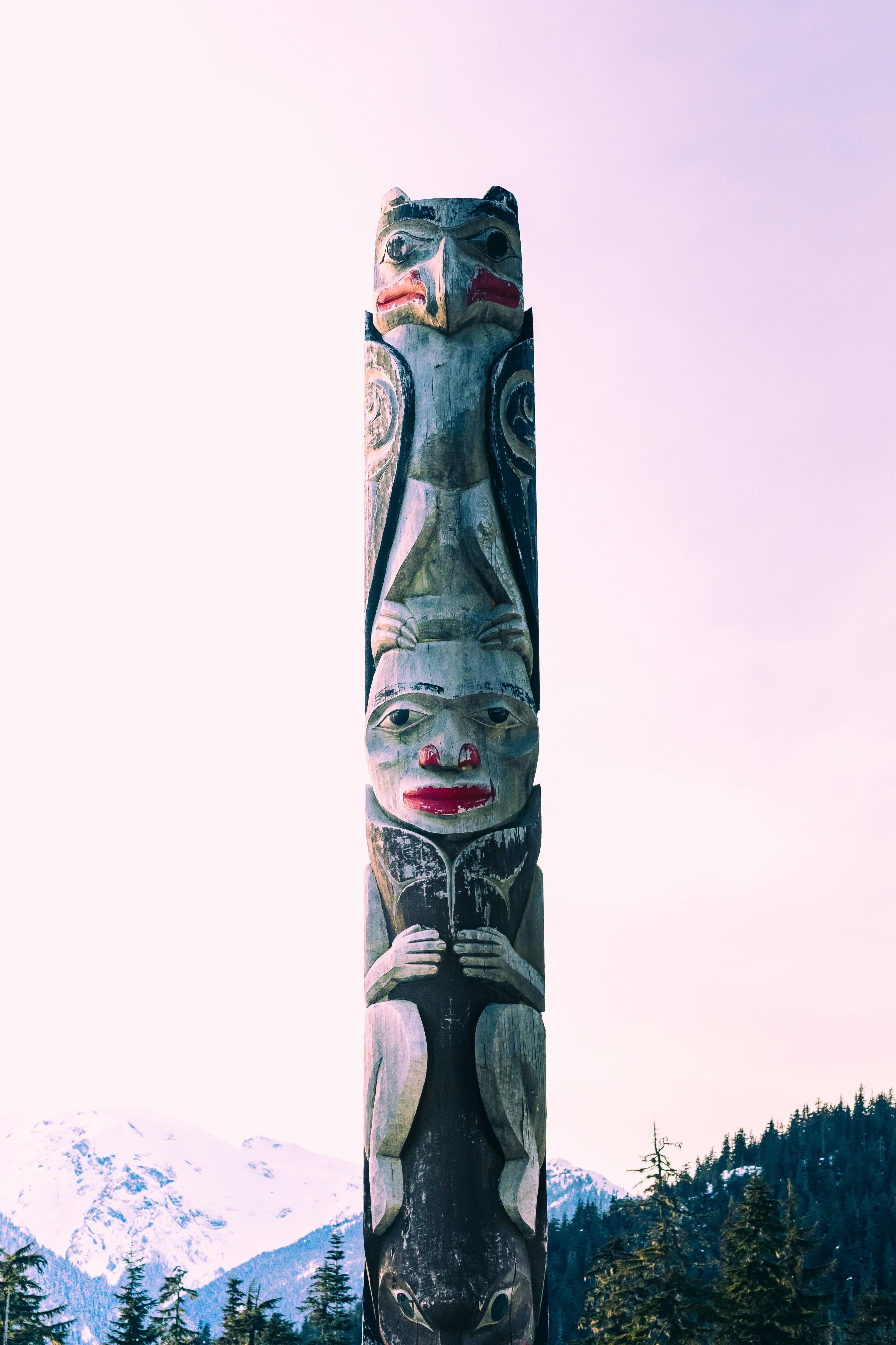 A traditional Indigenous totem pole with snowy mountains in the background, representing cultural heritage and connection to the land.